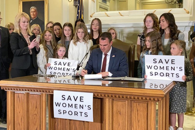 FILE - Oklahoma Gov. Kevin Stitt, center, signs a bill that prevents transgender girls and women from competing on female sports teams, March 30, 2022, in Oklahoma City. A new rule from President Joe Biden's administration assuring transgender students be allowed to use the school bathrooms that align with their gender identity could conflict with laws in Republican-controlled states that seek to make sure they can't. (AP Photo/Sean Murphy, File)
