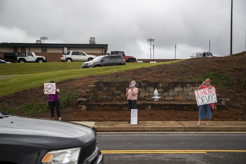 Protesters hold signs as the motorcade of U.S. Secretary of Education Betsy DeVos passes them following a visit to Forsyth Central High School in Cumming, Tuesday, August 25, 2020. (ALYSSA POINTER / ALYSSA.POINTER@AJC.COM)