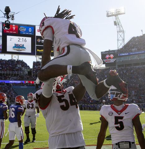 10/30/21 - Jacksonville -  Georgia Bulldogs running back James Cook (4) is lifted by  Georgia Bulldogs offensive lineman Justin Shaffer (54) after he scored the first TD during the first half of the annual NCCA  Georgia vs Florida game at TIAA Bank Field in Jacksonville.   Bob Andres / bandres@ajc.com