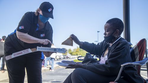 10/13/2020 - Lawrenceville, Georgia - Elaine Scarlett of Lawrenceville takes a free slice of pizza from a DominoÕs Pizza employee as she waits in line to cast her ballot on the second day of early voting at the Gwinnett County Voter Registration and Elections building in Lawrenceville, Tuesday, October 13, 2020.  (Alyssa Pointer / Alyssa.Pointer@ajc.com)