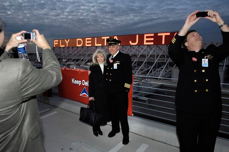 070131 - ATLANTA, GA -- Delta employees and executives celebrate the re-lighting of an Atlanta landmark, the "Fly Delta Jets" sign, which broke several years ago. The sign is located at the company's technical operations center at Hartsfield Jackson International Airport. Although the event was planned prior to today's announcement that US Airways is withdrawing its takeover bid, in its own way, the event marks a positive direction for the troubled Atlanta airline. Pictured getting their picture taken in front of the sign is Delta pilot Capt. Art Williams with Kathy Hunt, with the Delta pilots union. Right is Delta First Officer William Kessler (cq). (RICH ADDICKS / AJC staff)