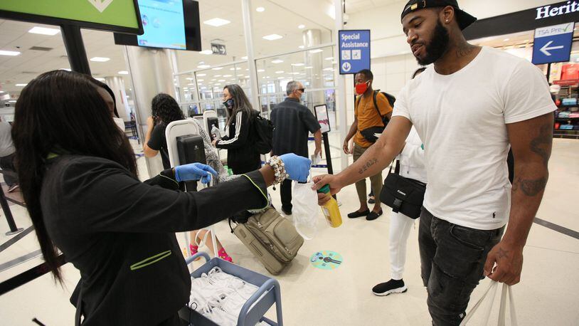 A Hartsfield-Jackson Airport staff person hands out face masks to passengers entering the security line in the airport’s South Terminal. Tuesday, June 23, 2020. Miguel Martinez for The Atlanta Journal-Constitution