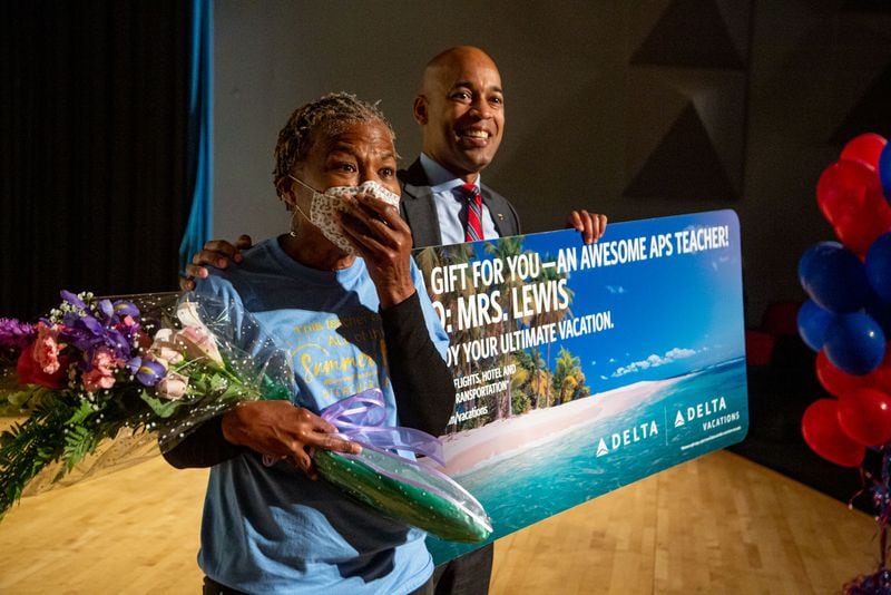 Mays High School teacher Sonja Lewis standing next to 
Shawn Cole, vice president of global sales for Delta Air Lines, reacts after learning she won a free trip including airfare and hotel accommodations to any Delta Vacations destination within the United States, Mexico, or the Caribbean on Friday, May 7, 2021.  STEVE SCHAEFER FOR THE ATLANTA JOURNAL-CONSTITUTION