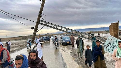 People pass by a damaged electric pole caused by flooding due to heavy rains near Chaman area, Pakistan, Thursday, April 18 2024. Lightning and heavy rains led to 14 deaths in Pakistan, officials said Wednesday, bringing the death toll from four days of extreme weather to at least 63, as the heaviest downpour in decades flooded villages on the country's southwestern coast. Flash floods have also killed dozens of people in neighboring Afghanistan. (AP Photo/Habib Ullah)