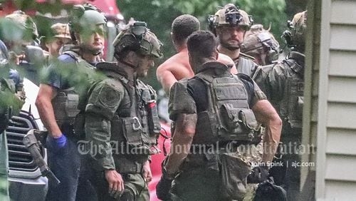 A man is led away from an Austell-area home in handcuffs Monday morning after an hourslong SWAT operation.