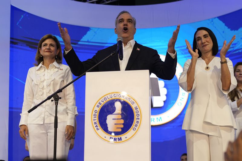Incumbent presidential candidate Luis Abinader, center, addresses supporters alongside vice presidential candidate Raquel Peña, left, and wife, Raquel Arbaje, after the first vote count showed him leading in general elections in Santo Domingo, Dominican Republic, Sunday, May 19, 2024. (AP Photo/Matias Delacroix)