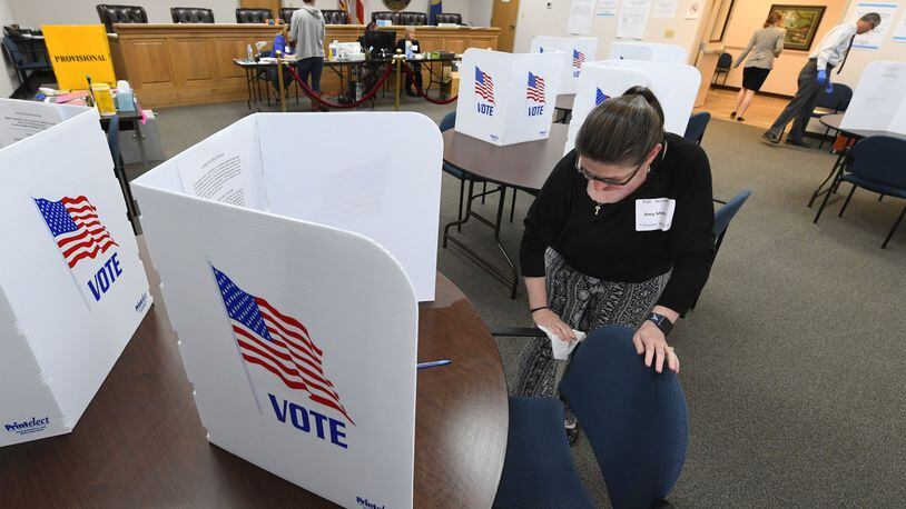Poll worker Amy Morris wipes down an area used by a voter during special election voting at city hall to fill an empty city council seat on Tuesday, March 24, 2020, in Dacula. The voting happens to on a day that was supposed to be the test run for the state’s new election system before coronavirus COVID-19 caused it to be called off. The city uses paper ballots and doesnt forsee switching to the new sytem because the machines are not given to municipalities for special elections.