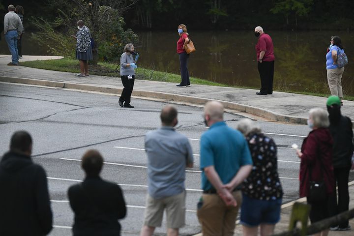 Poll worker Joan Edgar shouts instructions to voters in a long line that snakes around the parking lot during the first day of early voting on Monday, Oct. 12, 2020, at the Mountain Park Activity Building in Stone Mountain. JOHN AMIS FOR THE ATLANTA JOURNAL- CONSTITUTION