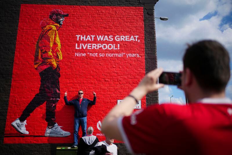 A fan poses for photos next to a mural with the image of Liverpool’s manager Jurgen Klopp prior to the English Premier League soccer match between Liverpool and Tottenham Hotspur at Anfield Stadium in Liverpool, England, Sunday, May 5, 2024. (AP Photo/Jon Super)