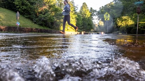 A runner crosses the water-soaked intersection of Chamblee Dunwoody Road and Dunwoody Knoll Drive, where a large water main break shut down the road Monday morning.
