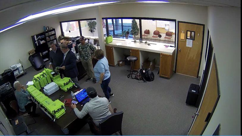 Surveillance video of the Coffee County elections office shows green voter check-in tablets, called PollPads, on a table while tech experts and supporters of then-President Donald Trump examined elections equipment on Jan. 7, 2021. 
From left: Coffee County Republican Party Chairwoman Cathy Latham (seated), Paul Maggio of SullivanStrickler, bail bondsman Scott Hall, county elections board member Eric Chaney, an unnamed analyst, and county Elections Director Misty Hampton. Source: Coffee County