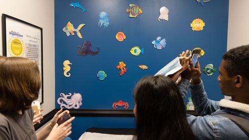 Lakeside High School Art Club members take pictures of the sea creatures they made hanging on a blue wall of a pediatric exam room at the Atlanta Urgent Care nearby. PHIL SKINNER FOR THE ATLANTA JOURNAL-CONSTITUTION
