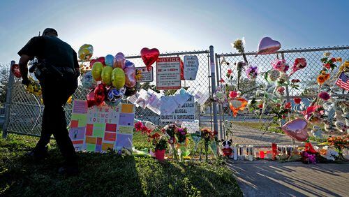A Broward County Sheriff's Office deputy removes police tape from a makeshift memorial at Marjory Stoneman Douglas High School in Parkland, Fla., Sunday, Feb. 18, 2018. Nikolas Cruz, a former student, was charged with 17 counts of premeditated murder on Thursday. (John McCall/South Florida Sun-Sentinel via AP)