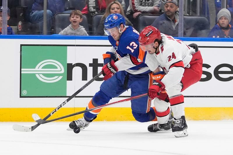 Carolina Hurricanes' Seth Jarvis (24) fights for control of the puck with New York Islanders' Mathew Barzal (13) during the first overtime period of Game 4 of an NHL hockey Stanley Cup first-round playoff series Saturday, April 27, 2024, in Elmont, N.Y. (AP Photo/Frank Franklin II)