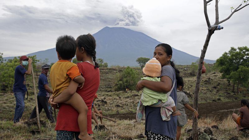 Villagers watch the Mount Agung volcano spew smoke and ashes in a filed in Karangasem, Bali, Indonesia, Wednesday, Nov. 29, 2017. The volcano with a deadly history on Indonesia's Bali, one of the world's most popular resort islands, has spewed ash 7,600 meters (4.7 miles) high and closed the island's international airport for a third day Wednesday. (AP Photo/Firdia Lisnawati)