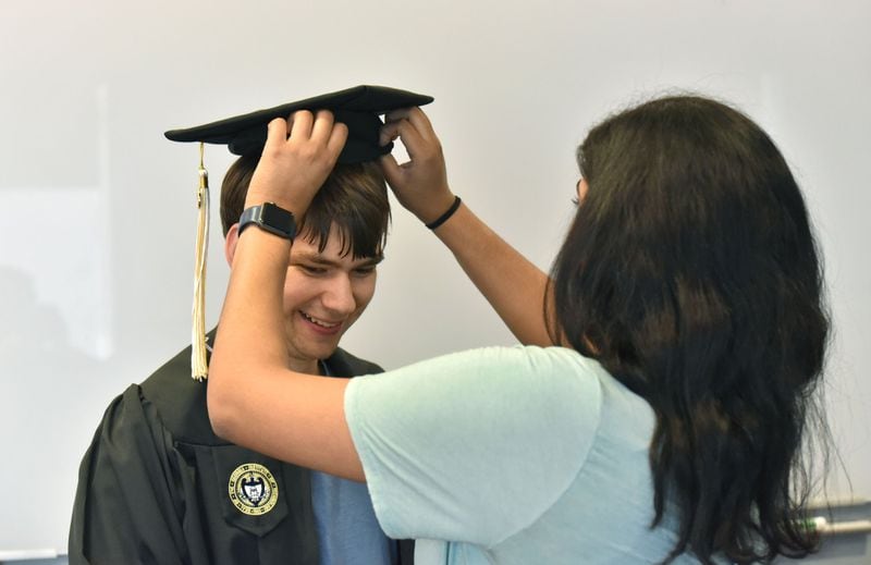 Kurt Vogel tries on his cap and gown as Ankita Raghupathy, right, teaching assistant, helps during a graduation rehearsal of the EXCEL program for students with intellectual disabilities at Georgia Tech’s Scheller College of Business. 