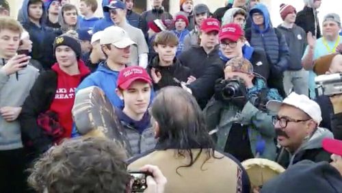 In this Friday, Jan. 18, 2019 image made from video provided by the Survival Media Agency, a teenager wearing a "Make America Great Again" hat, center left, stands in front of an elderly Native American singing and playing a drum in Washington. The Roman Catholic Diocese of Covington in Kentucky is looking into this and other videos that show youths, possibly from the diocese's all-male Covington Catholic High School, mocking Native Americans at a rally in Washington. (Survival Media Agency via AP)