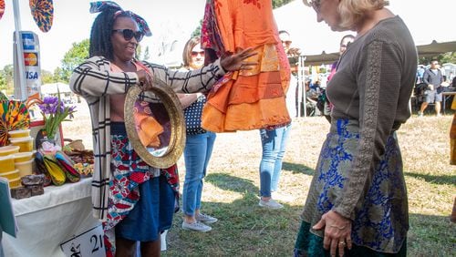 Rejoyce Dablah (R) helps a customer pick out one of her dresses from Ghana during the Johns Creek International Festival on October 23, 2021.  STEVE SCHAEFER FOR THE ATLANTA JOURNAL-CONSTITUTION