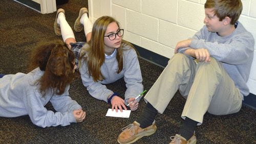 Eighth-grade students Sophia Gomez, Maddy Muir and Owen Daniel discuss random acts of kindness during a walk-in at Queen of Angels Catholic School. Instead of a walkout to protest school violence, the classmates used their 17 minutes to plan how to reach out to other students. CONTRIBUTED