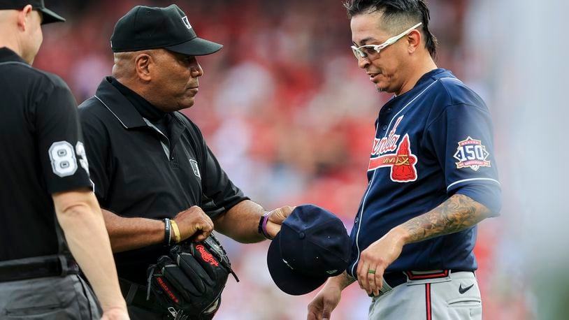 MLB umpire Laz Diaz, left, inspects the hat and glove of Atlanta Braves' Jesse Chavez after the first inning of a baseball game against the Cincinnati Reds in Cincinnati, Thursday, June 24, 2021. (AP Photo/Aaron Doster)