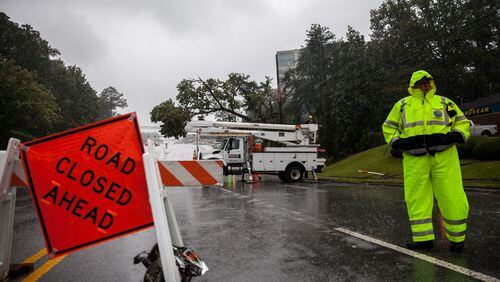 An officer keeps watch as crews work to clear a tree that fell on power lines on Hammond Drive Monday in Sandy Springs, Ga. BRANDEN CAMP/SPECIAL AJC FILE PHOTO