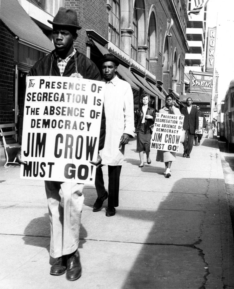 Marchers protest against segregation at Davison's department store in February 1961, displaying placards opposing Jim Crow laws as they walk on the sidewalk fronting Peachtree Street.
