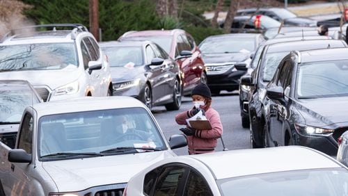 Janai Kornegay hands out forms while working at the Viral Solutions drive-thru COVID testing site Tuesday in Decatur. The line for testing stretched more than a block as people prepare for Christmas travel. (Ben Gray for The Atlanta Journal-Constitution)