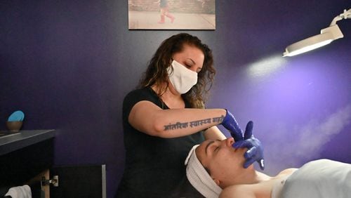 Paris Campeau gives a facial massage at Indigo Wellness Spa in Kirkwood on Wednesday to Virginia Carter, who asked that she wear latex gloves. Campeau, who owns the spa, didn’t open her boutique when the governor said she could a month ago, but now, with bills piling up and some clients ready to come by, she’s giving it a shot. (Hyosub Shin / Hyosub.Shin@ajc.com)