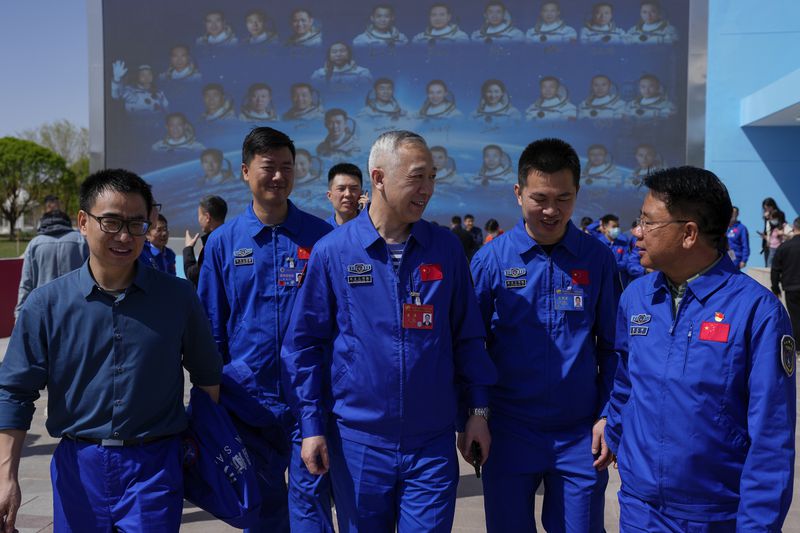 Staff members walk away from a billboard, background, depicting Chinese astronauts on past Shenzhou missions after Chinese astronauts for the upcoming Shenzhou-18 mission met with media members at the Jiuquan Satellite Launch Center in northwest China, Wednesday, April 24, 2024. (AP Photo/Andy Wong)