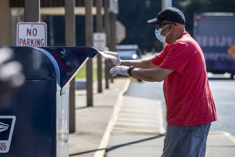 An individual deposits letters into a mailbox outside a post office in Decatur on Tuesday. The U.S. Postal Service, in a July 29 letter to Georgia Secretary of State Brad Raffensperger, recommended that voters request an absentee ballot at least 15 days before Election Day, and that they mail completed ballots at least one week in advance, by Oct. 27. (ALYSSA POINTER / ALYSSA.POINTER@AJC.COM)