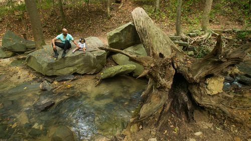 Uriel Ali, of Charleston, South Carolina, and his 1-year-old daughter Aryana sit next to a small creek  in Sandy Springs. Beginning this month, the city will evaluate all of its streams and creeks with the help of a Roswell firm.