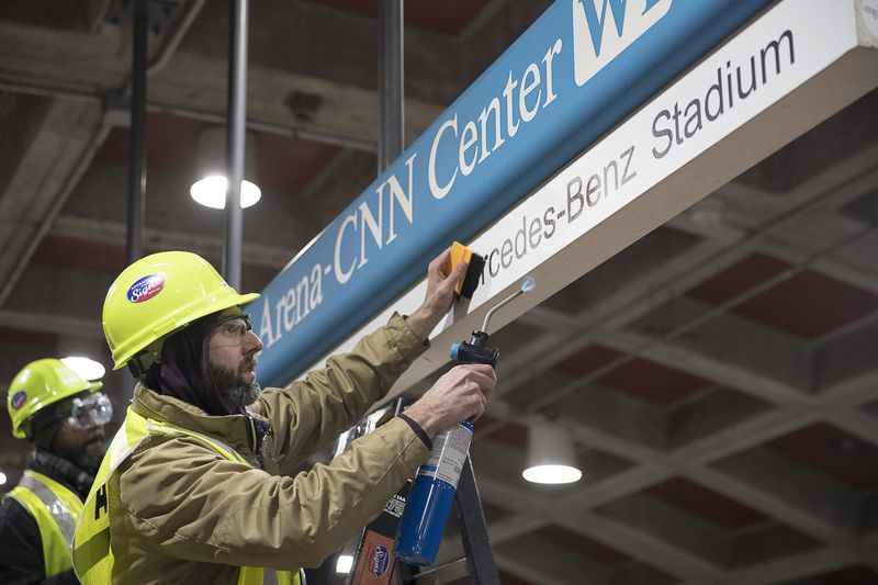 Tim Carl (second from left) of Advantage Graphics & Signs uses a torch to ensure the cohesiveness of the new Mercedes-Benz signage at the  MARTA Dome/GWCC/Philips Arena/CNN Center Transit in Atlanta, Wednesday, Jan. 16, 2019. Advantage Graphics & Signs worked in the transit station on Wednesday to replace signage that mislabeled Atlanta's two newly named sport stadiums. (Alyssa Pointer/Alyssa.Pointer@ajc.com)