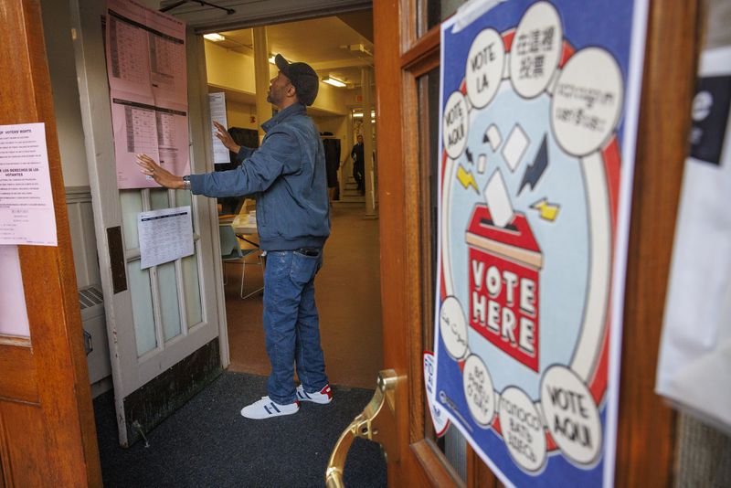 Christopher Coleman, committee person, hangs voter information on doors leading to polling station inside the Free Library Falls of Schuylkill Branch in East Falls section of Philadelphia for the state's primary election, Tuesday, April 23, 2024, in Philadelphia. (Alejandro A. Alvarez/The Philadelphia Inquirer via AP)