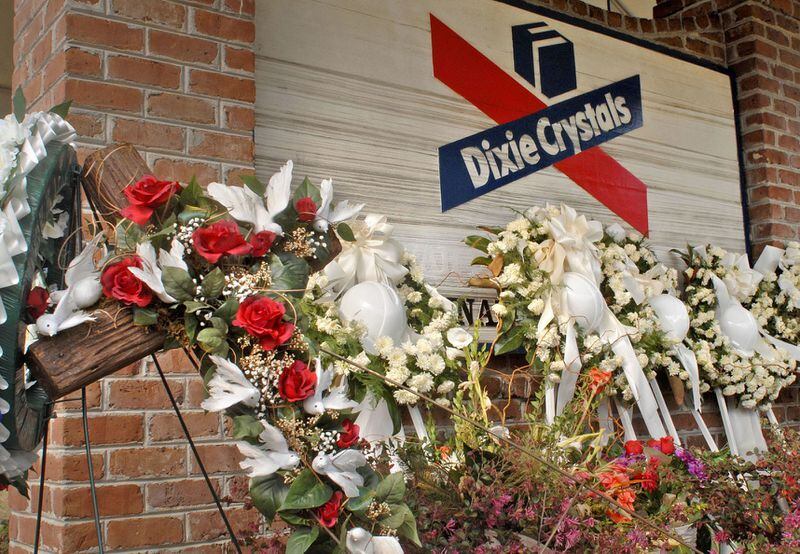Memorial flower arrangements with hard hats representing victims of the refinery explosion lay at the entrance to the Dixie Crystals plant.