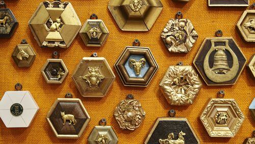 A collection of gold and wooden Museum Bees by Trace Mayer is nailed to an orange canvas. They are antique frames that are re-cut and a ornament such as a gilded bee is placed in the center. CONTRIBUTED BY Emily Followill Photography