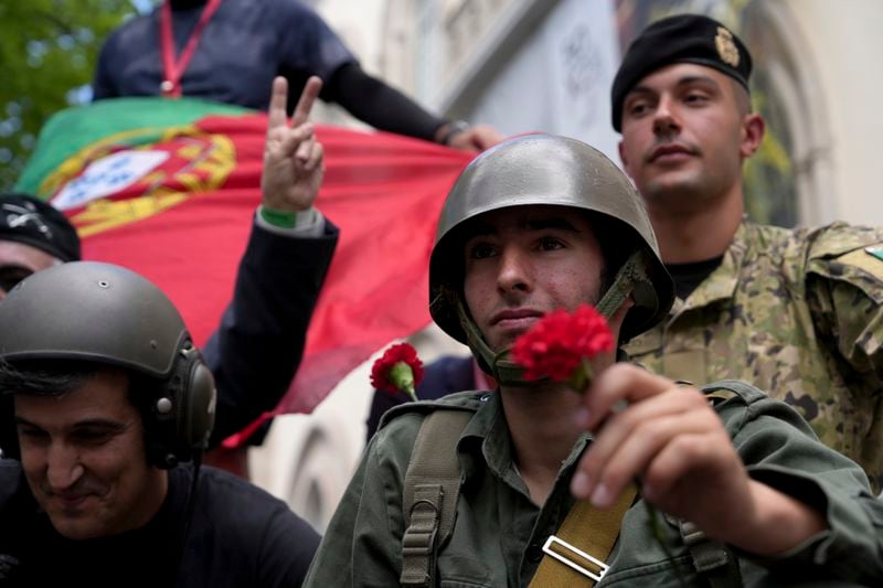 A soldier in 1974 uniform holds a red carnation at Carmo square in Lisbon, Thursday, April 25, 2024, during the reenactment of troops movements, part of anniversary celebrations of the Carnation Revolution. The army led coup restored democracy in Portugal after 48 years of a fascist dictatorship. (AP Photo/Ana Brigida)